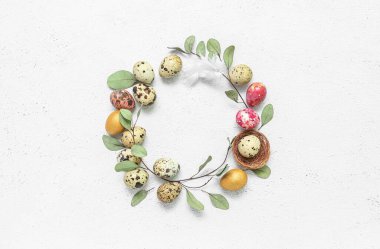 Frame made of Easter quail eggs, feather and eucalyptus branches on white background