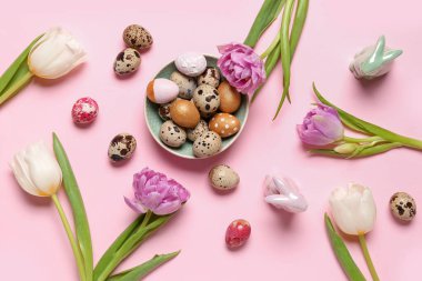 Composition with plate of Easter quail eggs, bunnies and tulip flowers on pink background
