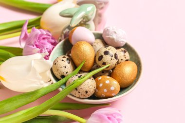 Plate of Easter quail eggs, bunny and tulip flowers on pink background, closeup