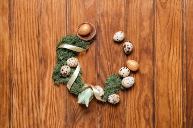 Frame made of Easter quail eggs, bunny and moss on brown wooden background