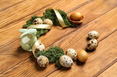 Frame made of Easter quail eggs, bunny and moss on brown wooden background