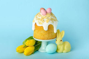 Stand with Easter cake, tulip flowers and bunny on blue background