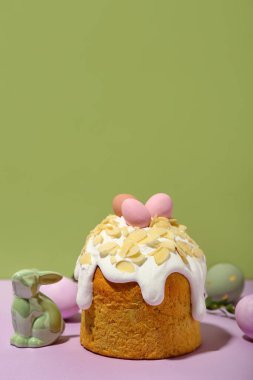 Easter cake, painted eggs and bunny on lilac table against green background