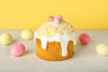 Easter cake and painted eggs on table near yellow wall