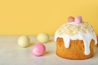 Easter cake and painted eggs on table near yellow wall