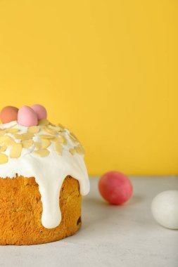 Easter cake and painted eggs on table near yellow wall