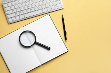 Blank open book, magnifier, keyboard and pen on yellow background. World Poetry Day celebration