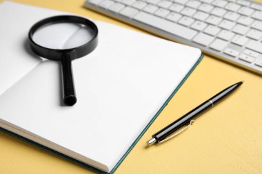 Blank open book, magnifier, pen and keyboard on yellow background, closeup. World Poetry Day celebration