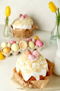 Easter cake with painted eggs and tulip flowers on table near white wall