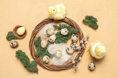 Composition with Easter quail eggs, baby chickens and wreath on beige background
