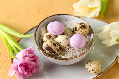 Bowl with Easter quail eggs and tulip flowers on beige table