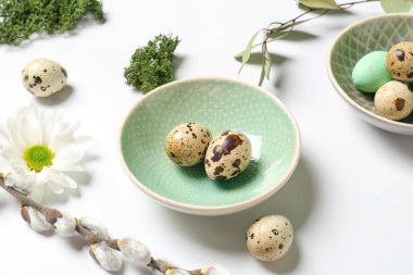 Plate with Easter quail eggs and chamomile flower on white background