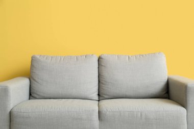 Stylish grey sofa near yellow wall