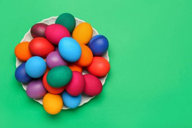 Plate with colorful Easter eggs on green background