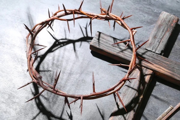 Crown of thorns with wooden cross on dark background, closeup. Good Friday concept