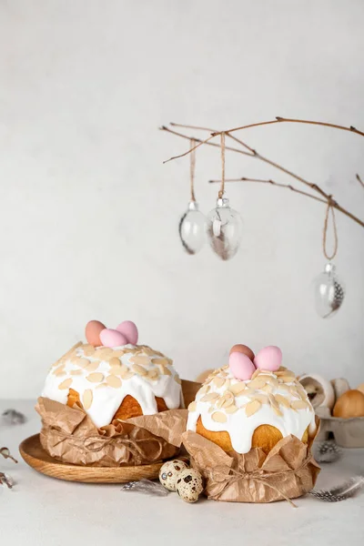 Easter cakes with painted eggs and feathers on table near white wall