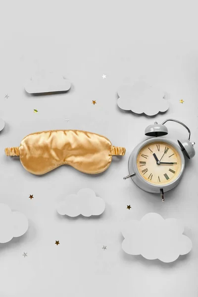 Composition with sleeping mask, alarm clock, paper clouds and confetti on light background. World Sleep Day concept