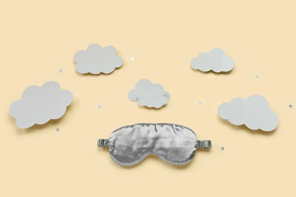Composition with sleeping mask, paper clouds and confetti on color background. World Sleep Day concept