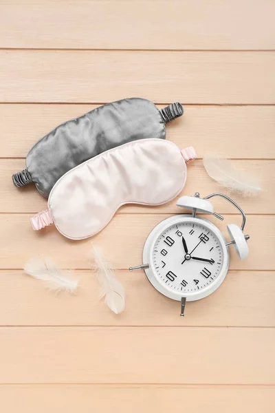 Sleeping masks, alarm clock and feathers on color wooden background. World Sleep Day concept