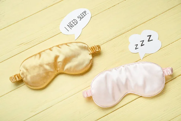 Sleeping masks and speech bubbles on color wooden background. World Sleep Day concept
