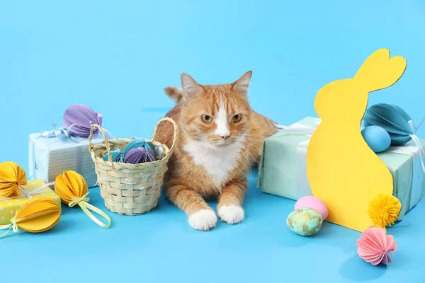 Cute cat with Easter eggs, gifts and paper rabbit on blue background