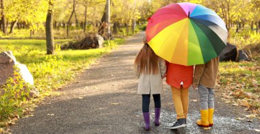 Cute little children with umbrella walking in autumn park, back view