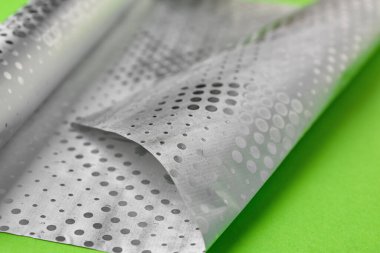 Sheet of aluminium foil on green background, closeup