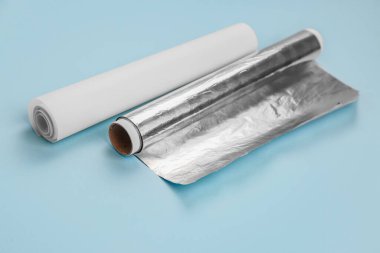 Rolls of aluminium foil and baking paper on blue background