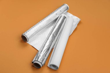 Rolls of aluminium foil and baking paper on orange background