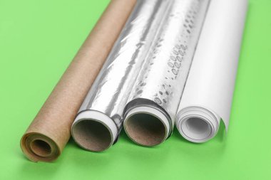 Rolls of aluminium foil and baking paper on green background, closeup