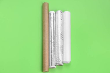 Rolls of aluminium foil and baking paper on green background