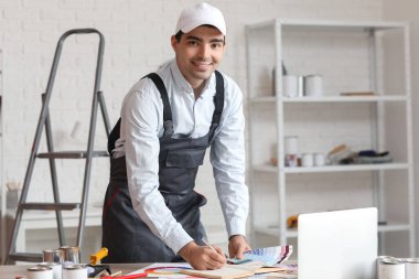 Male painter with color palettes writing in notebook at table