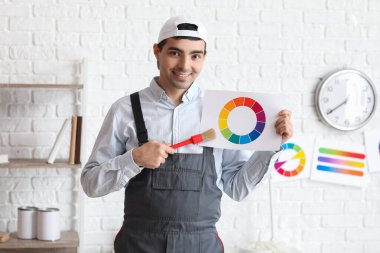 Male painter with color palette and brush in room