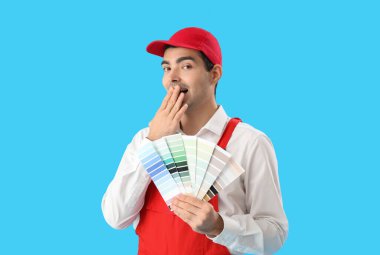 Surprised male painter with color palettes on blue background