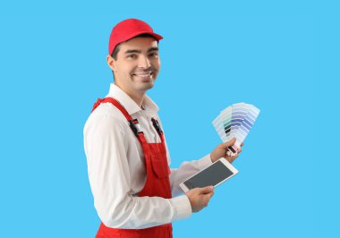 Male painter with color palettes and tablet computer on blue background