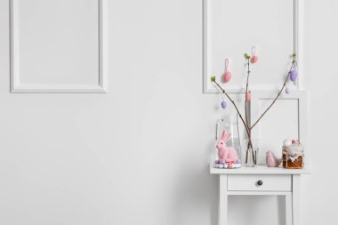 Beautiful Easter decor, cake and jug of water on table near light wall