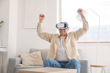 Mature man in VR glasses sitting on sofa at home