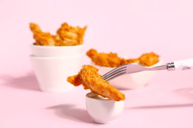 Fork with tasty nugget and sauce on pink background