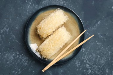 Plate with raw rice noodles and chopsticks on dark background