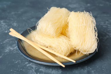 Plate with raw rice noodles and chopsticks on dark background