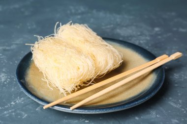 Plate with raw rice noodles and chopsticks on dark background