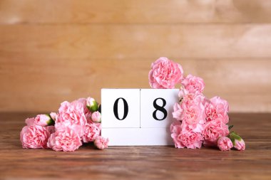 Cube calendar with date MARCH 8 and beautiful carnation flowers on wooden table. Women's Day celebration