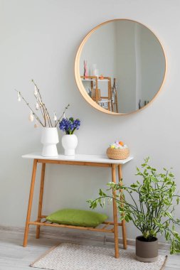 Vases with tree branches, flowers and Easter eggs on table in living room