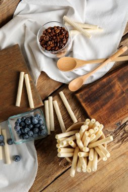 Bowls with delicious wafer rolls, blueberries and coffee beans on wooden table
