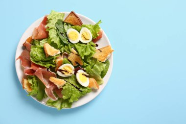 Plate of delicious salad with boiled eggs and jamon on blue background