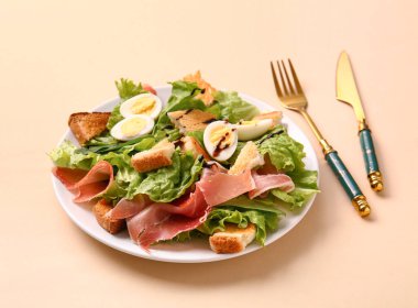 Plate of delicious salad with boiled eggs and jamon on beige background