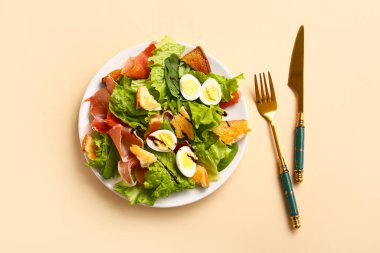 Plate of delicious salad with boiled eggs and jamon on beige background