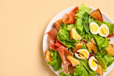 Plate of delicious salad with boiled eggs and jamon on beige background