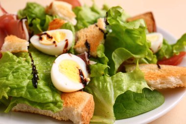 Plate of delicious salad with boiled eggs and jamon on beige background