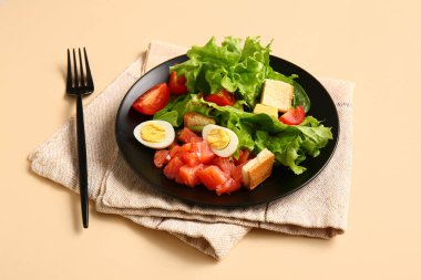 Plate of delicious salad with boiled eggs and salmon on beige background
